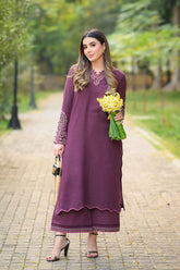 Woman in a purple outfit holding yellow flowers on a path with greenery.