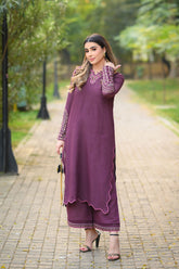 Woman in a purple traditional outfit standing on a pathway with greenery in the background