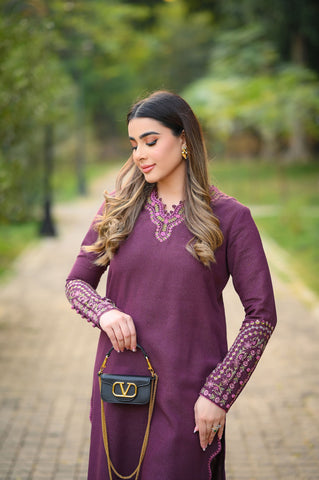 Woman in a purple dress holding a black handbag with a blurred green background